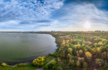 Autumn forest on lake shore at sunset and city on horizon, aerial view. Lake Shartash and Yekaterinburg, Russiaの写真素材