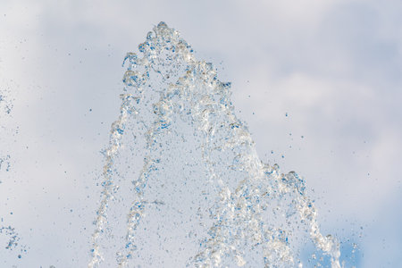 Splashes of water against light background. Fountain, a jet of water against cloudy sky.の写真素材