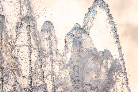 Splashes of water against light background. Fountain, a jet of water against cloudy sky.の写真素材