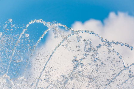 Splashes of water against light background. Fountain, a jet of water against cloudy sky.