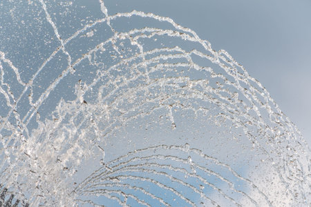 Splashes of water against light background. Fountain, a jet of water against cloudy sky.の写真素材