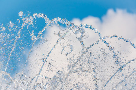 Splashes of water against light background. Fountain, a jet of water against cloudy sky.の写真素材