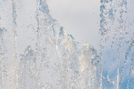 Splashes of water against light background. Fountain, a jet of water against cloudy sky.の写真素材