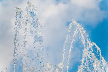 Splashes of water against light background. Fountain, a jet of water against cloudy sky.