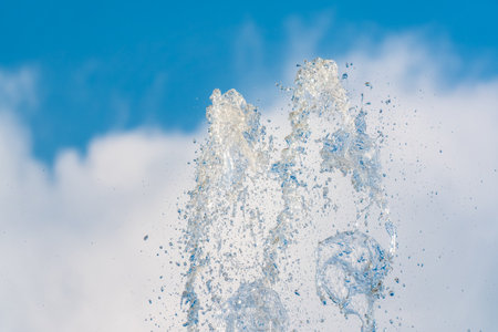 Splashes of water against light background. Fountain, a jet of water against cloudy sky.の写真素材