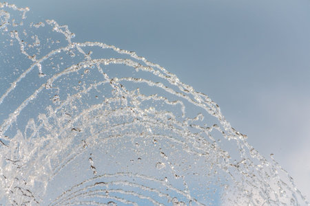 Splashes of water against light background. Fountain, a jet of water against cloudy sky.