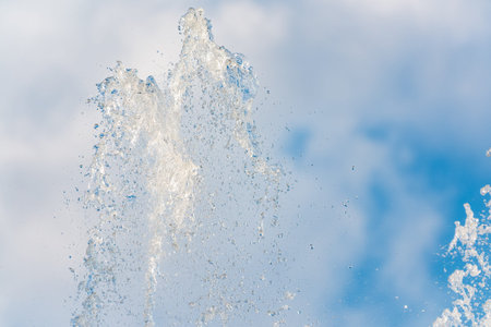 Splashes of water against light background. Fountain, a jet of water against cloudy sky.