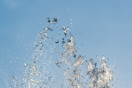 Splashes of water against light background. Fountain, a jet of water against cloudy sky.