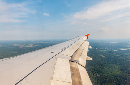 View of airplane wing, blue skies and green land during landing. Airplane window view. Earth and sky...