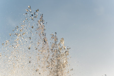 Splashes of water against light background. Fountain, a jet of water against cloudy sky.
