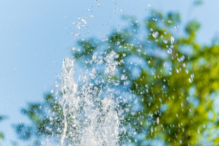 Splashes of water against light background. Fountain, a jet of water against cloudy sky.