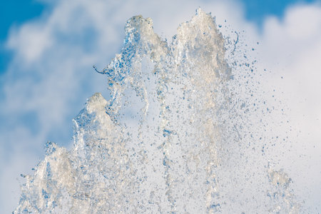 Splashes of water against light background. Fountain, a jet of water against cloudy sky.の写真素材