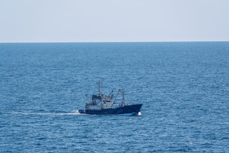 Fishing boat in blue sea and clear sky with birds flying overhead. Calm blue sea with the silhouette...