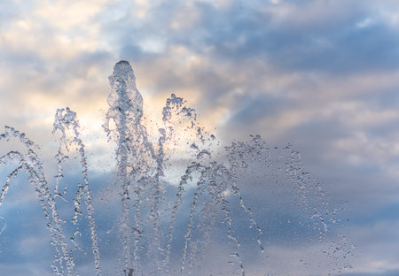 Splashes of water against light background. Fountain, a jet of water against cloudy sky.の写真素材