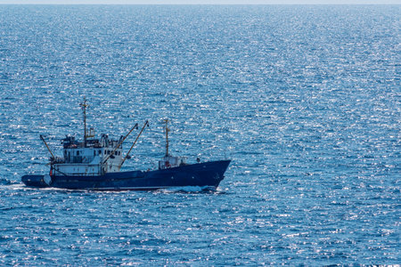Fishing boat in blue sea and clear sky with birds flying overhead. Calm blue sea with the silhouette of a ship on the horizonの写真素材