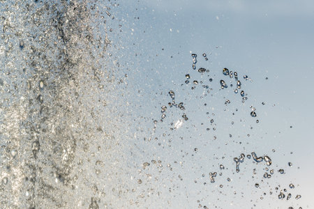 Splashes of water against light background. Fountain, a jet of water against cloudy sky.の写真素材