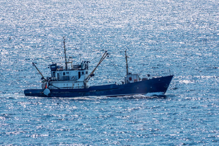 Fishing boat in blue sea and clear sky with birds flying overhead. Calm blue sea with the silhouette of a ship on the horizonの写真素材