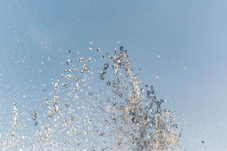 Splashes of water against light background. Fountain, a jet of water against cloudy sky.の写真素材