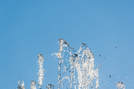 Splashes of water against light background. Fountain, a jet of water against cloudy sky.の写真素材