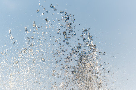 Splashes of water against light background. Fountain, a jet of water against cloudy sky.の写真素材