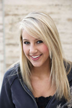Attractive young woman in a gray hoodie smiles towards the camera while standing outside. Vertical shot.の写真素材