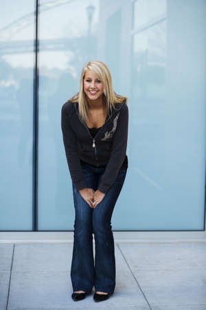 Attractive young woman in a sweatshirt and jeans stands smiling with her hands in her lap. Vertical shot.の写真素材