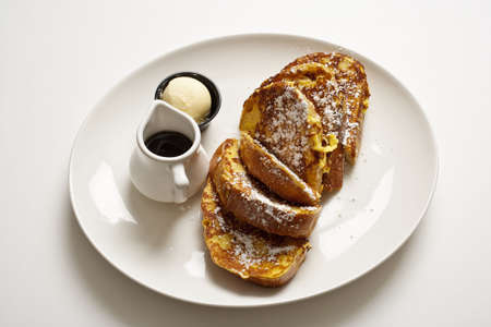 Plate of French toast on a plain white table. A scoop of butter and syrup is on the side. Horizontal shot.の写真素材