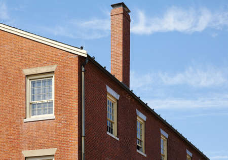 Low angle view of a brick building against a clear blue sky. A chimney is jutting out of the roof. Horizontal shot.の写真素材