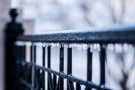 Closeup of ice covered black wrought iron fence with tiny icicles hanging from railingの写真素材
