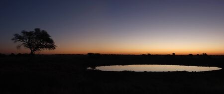 Panorama from two photos  Sunset view of the waterhole, Okaukeujo Rest Camp,  Etosha National Park, Namibiaの写真素材
