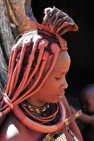 EPUPA, NAMIBIA - MAY 2011: An unknown Himba woman, with body colored in red ochre, poses for...