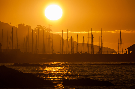 Silhouette of ships masts against sunset over the Gordons Bay harbor in the Western Cape Province of South Africaの写真素材