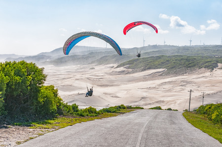 PORT ELIZABETH, SOUTH AFRICA - FEBRUARY 27, 2016: Silhouettes of two paragliders in the air against beach dunes at Beachview near Port Elizabethのeditorial素材