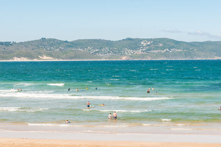 KNYSNA, SOUTH AFRICA - MARCH 3, 2016: Holiday-makers and surfers at a beach in Buffelsbaai (Buffalo Bay) with the small town of Brenton-On-Sea in the backのeditorial素材