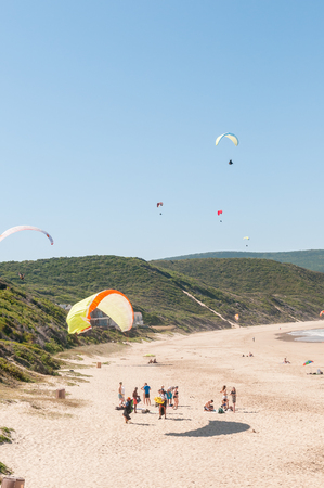 KNYSNA, SOUTH AFRICA - MARCH 3, 2016: Paragliders in the air while beachgoers enjoy the sun at a beach in Buffelsbaai (Buffalo Bay), a small town in the Knysna municipal areaのeditorial素材