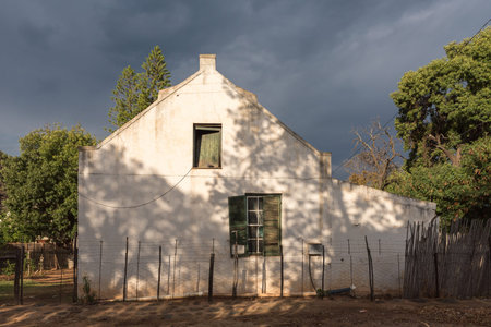 DE RUST, SOUTH AFRICA - MARCH 23, 2017: An historic old house in De Rust against a backdrop of dark cloudsのeditorial素材