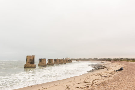 SWAKOPMUND, NAMIBIA - JUNE 30, 2017: An angler and pillars of the old railroad bridge over the mouth Swakop River with part of Swakopmund in the backのeditorial素材