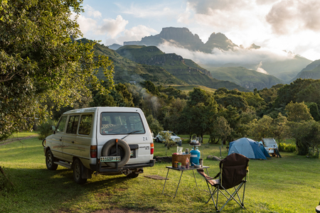 MONKS COWL, SOUTH AFRICA - MARCH 18, 2018: A tent and vehicles at the camping site at Monks Cowl in the Drakensberg. Cathedral peak (left) and Monks Cowl (right) are visible in the backのeditorial素材