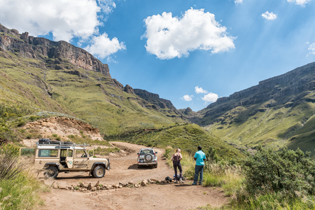 HIMEVILLE, SOUTH AFRICA - MARCH 24, 2018: Two unidentified tourists and four-wheel drive vehicles on the Sani Pass. The hairpin bends of the Sani Pass are visible in the backのeditorial素材