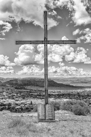 FICKSBURG, SOUTH AFRICA - MARCH 12, 2018:  A wooden cross with the Ten Commandments engraved on a granite scroll with the central business district of Ficksburg in the back. Monochromeのeditorial素材