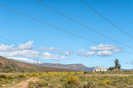 CERES, SOUTH AFRICA, AUGUST 8, 2018: Farm landscape at Karoopoort  on road R355 in the Western Cape Province. Yellow flowers, a house, electricity infrastructure and snow on Matroosberg are visibleのeditorial素材