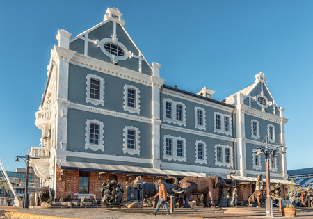 CAPE TOWN, SOUTH AFRICA, AUGUST 9, 2018: The historic Port Captains building at the Victoria and Alfred Waterfront in Cape Town in the Western Cape Province. Artwork for sale and a pedestrian are visibleのeditorial素材