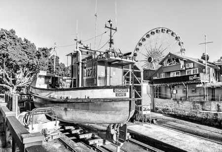 CAPE TOWN, SOUTH AFRICA, AUGUST 9, 2018:  A boat on dry ground at the Victoria and Alfred Waterfront in Cape Town in the Western Cape Province. A big wheel and the Sea Rescue Institute are visible. Monochromeのeditorial素材