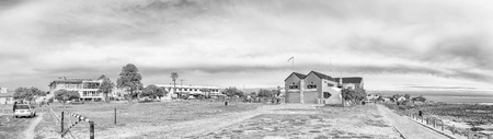MELKBOSSTRAND, SOUTH AFRICA, AUGUST 19, 2018: A beach scene, with restaurants, businesses and people, in Melkbosstrand in the Western Cape Province. The building of the National Sea Rescue Institute is visible. Monochromeのeditorial素材
