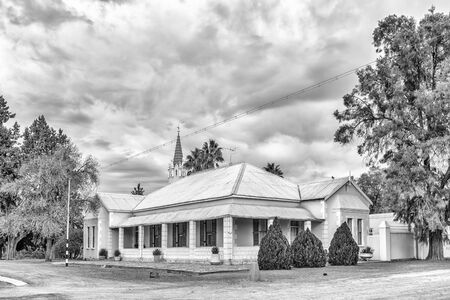 VOSBURG, SOUTH AFRICA, SEPTEMBER 1, 2018: The parsonage of the Dutch Reformed Church in Vosburg in the Northern Cape Province. The church is visible in the back. Monochromeのeditorial素材