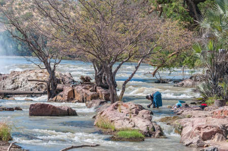 EPUPA, NAMIBIA - MAY 24, 2011: A woman washing clothes in the Kunene River at the top of the Epupa waterfallsのeditorial素材