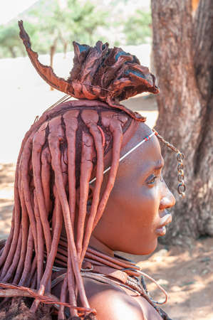 EPUPA, NAMIBIA - MAY 27, 2011: Profile of a married Himba woman with traditional hair locks and ornate headpiece posing for photographers at a Himba village near Epupaのeditorial素材