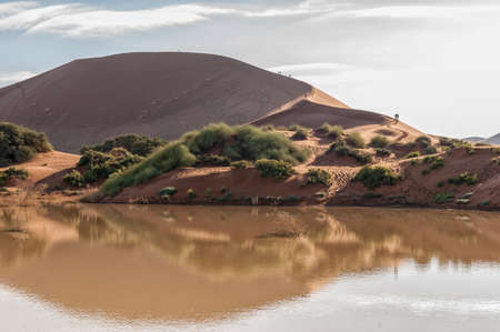 A view accross Sossusvlei, filled with water, and a sand dune with people on itの写真素材