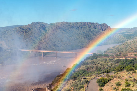 The single lane road bridge over the Orange River below the Gariep Dam. is visible behind a double rainbowの写真素材