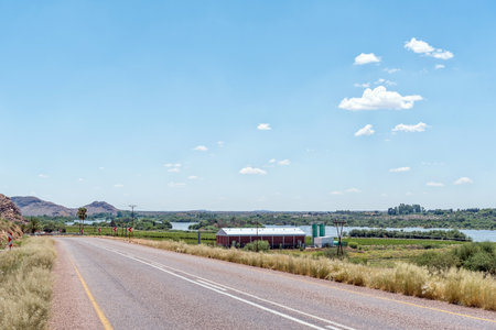 Upington, South Africa - Feb 24, 2023: A road scene, with buildings and the flooded Orange River, on road N10 near Leerkrans in the Northern Cape Provinceのeditorial素材